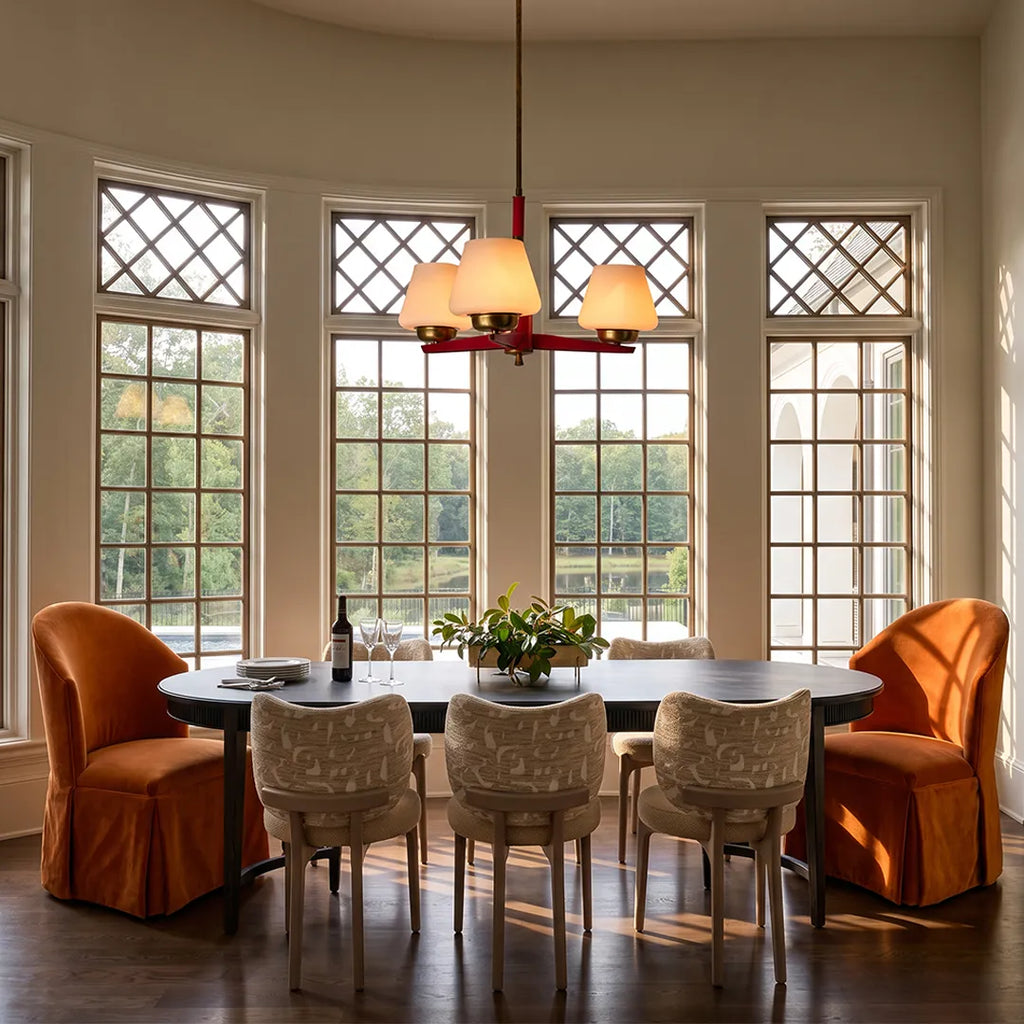 3 light chandeliers hanging over a dining table with decorative windows and warm neutral seating.