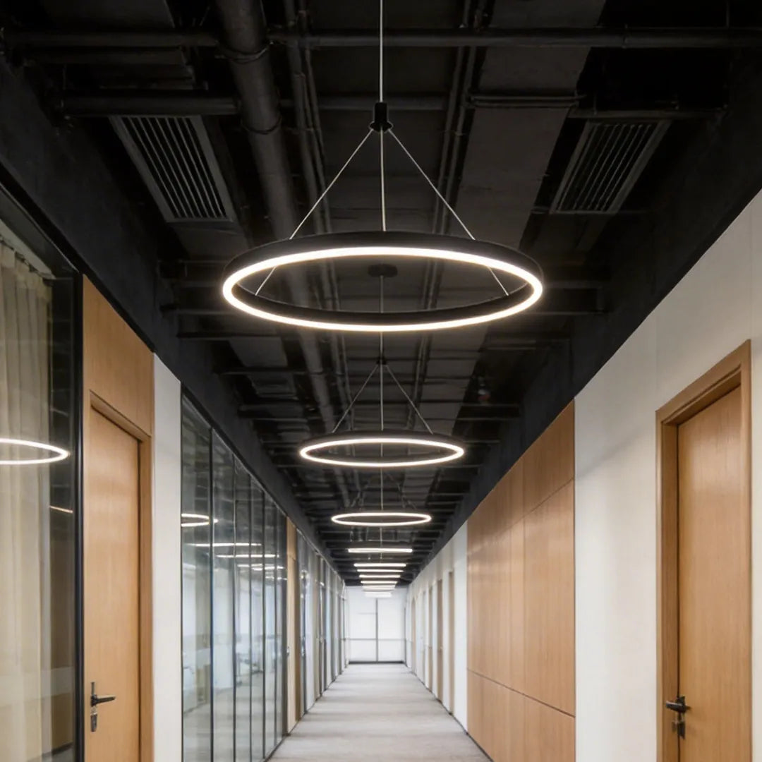 Ring metal chandelier installed in a contemporary office corridor with repeating circular fixtures along the ceiling.